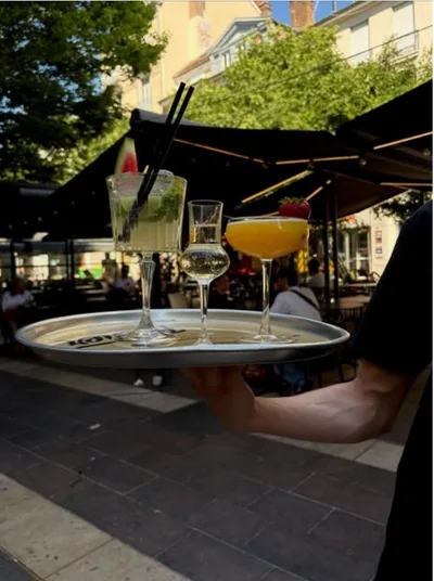 Un serveur porte un plateau avec deux cocktails, en terrasse